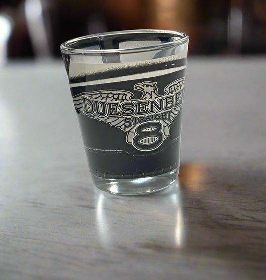 Clear shot glass with Duesenberg logo on a white surface