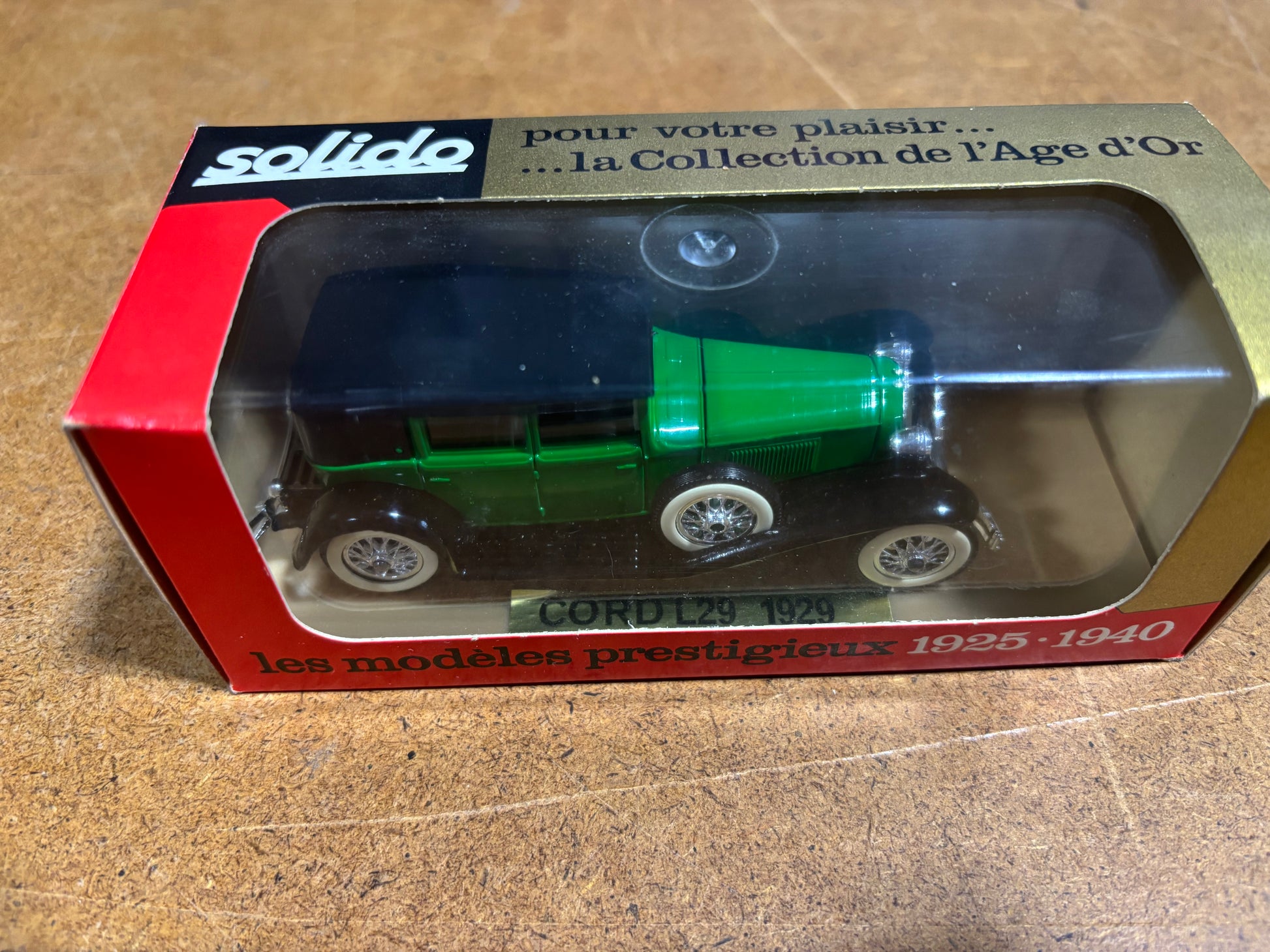 Green toy car in a Solido box on a wooden surface