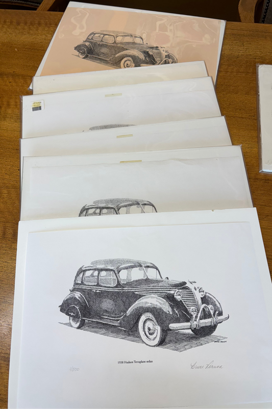Set of vintage car illustrations on paper sheets with a black case on a wooden surface.
